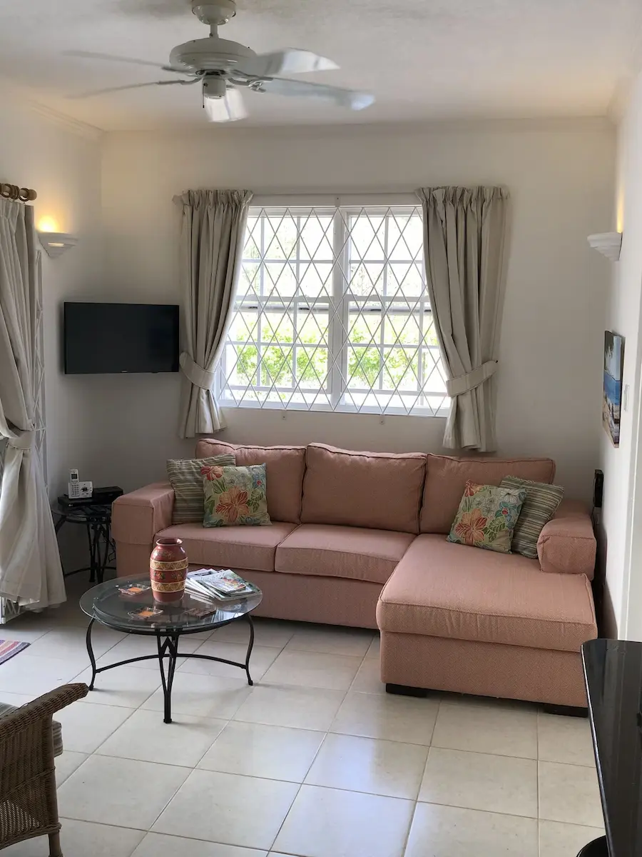 Bright open-plan lounge at 7 Springcourt with pink sectional sofa, ceiling fan and wall-mounted TV.