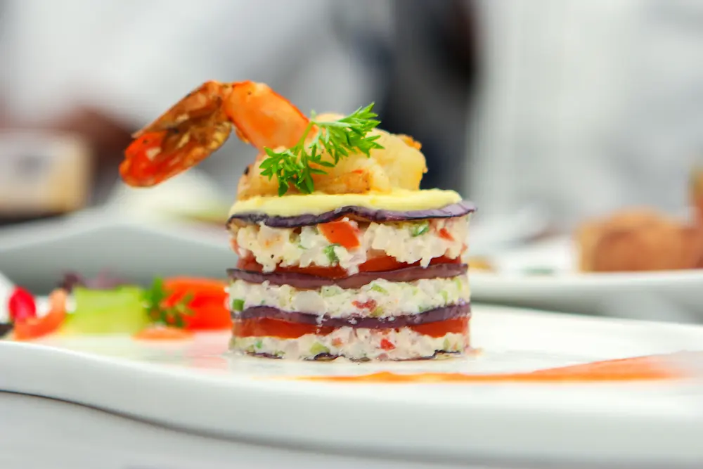 Elegantly plated Caribbean shrimp and vegetable tower dish with sauce garnish.
