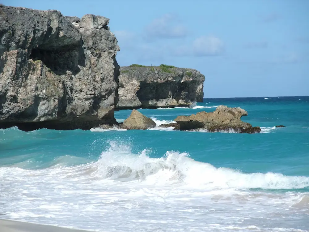 Dramatic Barbados coastline with turquoise waves crashing against weathered limestone cliffs.