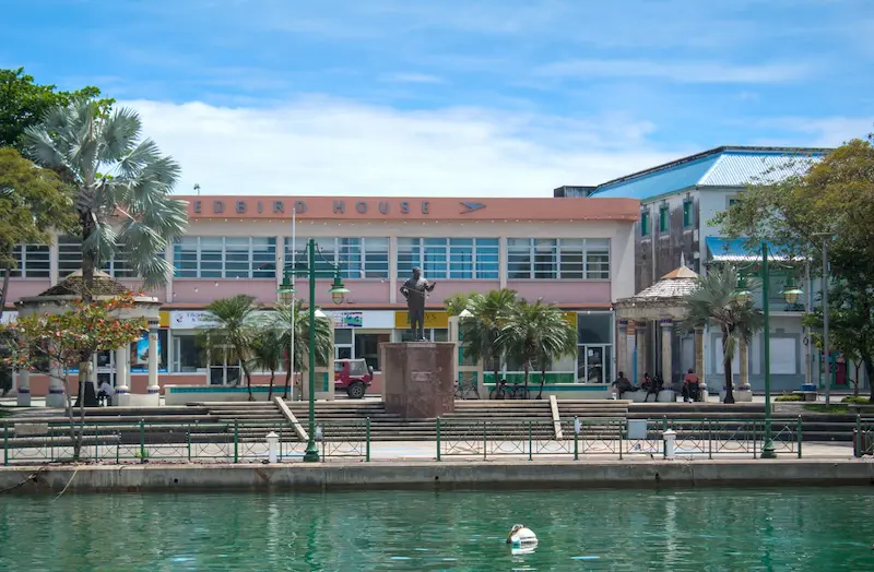 Bridgetown waterfront in Barbados with historic buildings, palm trees and a statue overlooking the careenage.